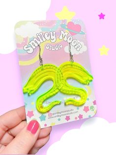 a pair of neon yellow earrings with the words smiley nose on it in front of a pink background