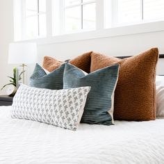 three pillows on top of a bed with white sheets and blue throw pillows in front of them