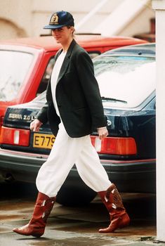 a woman walking down the street in white pants and cowboy boots