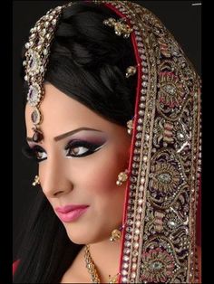 a woman wearing a red and gold bridal outfit with jewelry on her head, in front of a black background