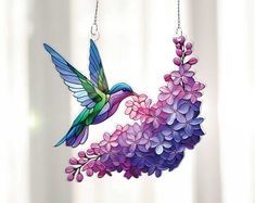 a hummingbird hanging from a chain with purple flowers