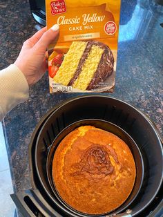 a person holding a box of cake mix next to a crock pot with a piece of cake in it