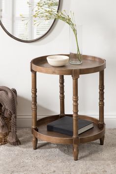 a round wooden table with a glass vase on top and a book next to it