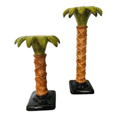 two ceramic palm trees on black bases with green leaves and brown trunks, one standing upright in front of the other