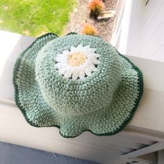 a crocheted hat sitting on top of a window sill next to a flower