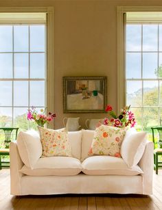 a white couch sitting in front of two windows with vases on top of it