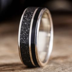 a wedding ring with black and silver inlays on the outside, sitting on top of a piece of wood