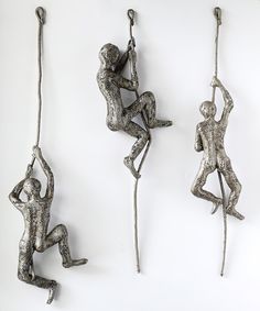 three metal figurines hanging from hooks on a white wall with one holding the other