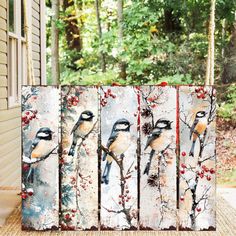 four birds painted on wooden boards sitting in front of a house with trees and bushes