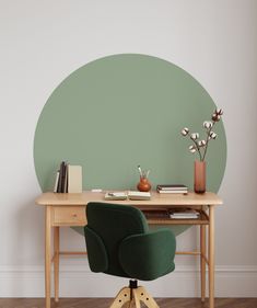 a desk with a chair, book and vase on it in front of a green circle wall