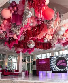 a room filled with lots of pink and red balloons hanging from the ceiling above it