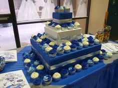 a blue and white wedding cake with cupcakes on the table next to it