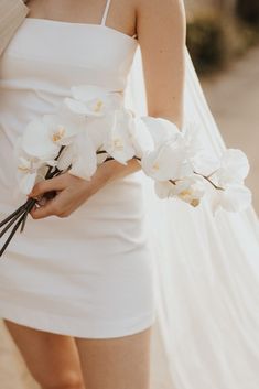 a woman in a white dress holding flowers on her left hand and the other hand behind her back