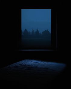 an empty bed in a dark room with the night sky visible through it's window