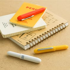 two notebooks and a pen sitting on top of a table next to each other