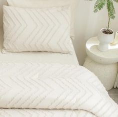 a white bed with two pillows and a plant on the side table next to it