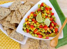 a bowl filled with corn and vegetables next to tortilla chips on a plate