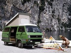 a green van parked next to a body of water with a surfboard in front of it