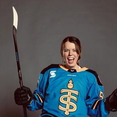 a female hockey player is smiling and holding her stick in one hand while posing for the camera