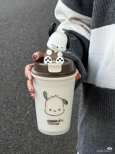 a woman is holding a cup with a small animal on it's lid, and she has her hand in the cup