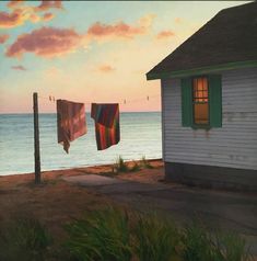 two towels hanging on a clothes line next to a house near the ocean at sunset