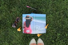 a book laying on top of a lush green field next to sunglasses and a pair of flip flops