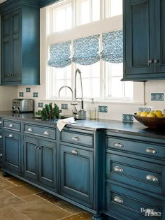 a kitchen with blue cabinets and tile flooring, along with a bowl of fruit on the counter