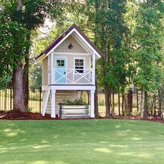 a small white house with a porch in the middle of some grass and trees behind it