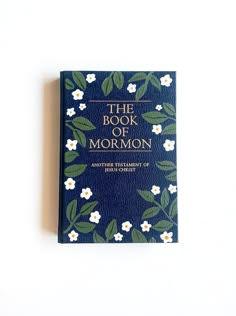 the book of mormon written in blue leather with white flowers and green leaves on it