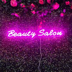 a neon sign that says beauty salon in front of some pink flowers and greenery