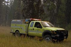 a yellow fire truck parked in the middle of a field with tall grass and trees