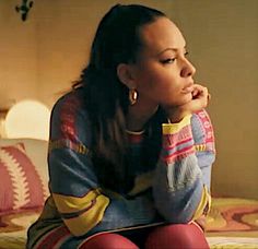 a young woman sitting on top of a bed next to a red and yellow pillow