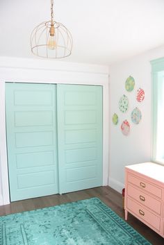 a bedroom with mint green doors and pink dresser in the corner, next to a blue rug