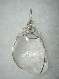 Clear Quartz Pendant Wire Wrapped in .925 Sterling Silver Round Wire This inspiring stone exhibits transparent clarity with multiple internal reflection and refraction with some iridescent display. As it is clear, reflecting and refracting any background color, it is very versatile and can be worn with any color of clothing; a non-standard shape, non-uniform surface, and internal crystal plane/fine fracture reflection and refraction make this stone of more appeal to an artistic view than a puris Elegant Silver Crystals For Gift, Elegant Silver Crystals As A Gift, Elegant Silver Crystals For Gifts, Elegant Silver Gemstone Crystals, Clear Quartz Gemstone Crystals, Handmade Elegant Silver Crystals, Silver Gemstone Crystals For Jewelry Making, Silver Quartz Crystals For Healing, Silver Healing Mineral Crystals