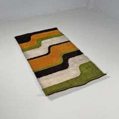 a rug is laying on the floor with white walls in the background and an orange, green, black, and yellow striped design