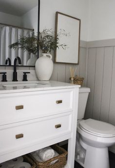 a white toilet sitting next to a sink in a bathroom under a mirror and framed pictures