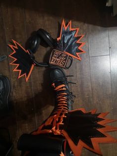 a pair of black and orange motorcycle boots on top of a wooden floor next to a wall