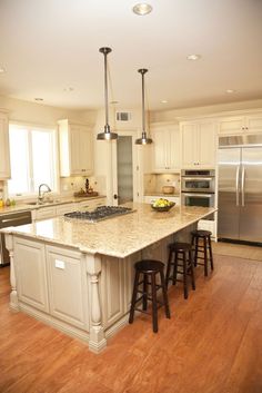 a large kitchen with an island in the middle and two stools at the end