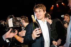 a man in a suit holding a bottle of wine and talking to someone on the camera