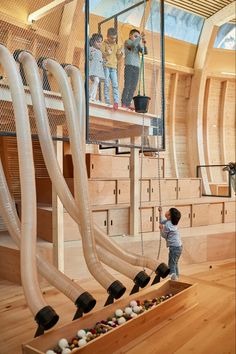 two children are playing in an open space with wooden floors and large pipes on the ceiling