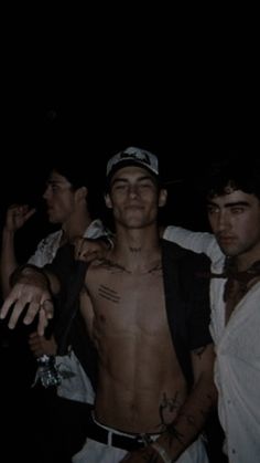 three men standing next to each other in the dark with one holding his shirt open