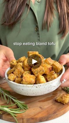 a woman holding a white bowl filled with food on top of a wooden cutting board