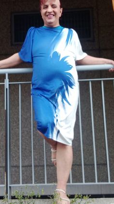 a woman in a blue and white dress standing on a balcony with her arms outstretched