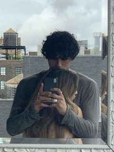 a man and woman taking a selfie in front of a mirror with buildings in the background