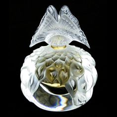 a glass object with a butterfly on it's head sitting on a black surface