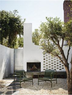 two green chairs sitting in front of a fire place next to a white wall and tree