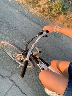 a woman riding a bike down a street next to a grass covered field and trees