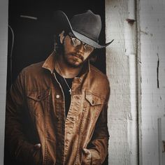 a man wearing a cowboy hat and glasses standing in front of a door with his hand on his hip