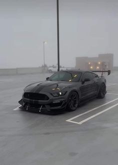 a black car parked in a parking lot on a foggy day with no one around