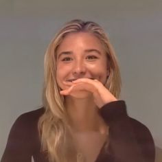 a woman with blonde hair is smiling and posing for the camera while holding her hands to her mouth